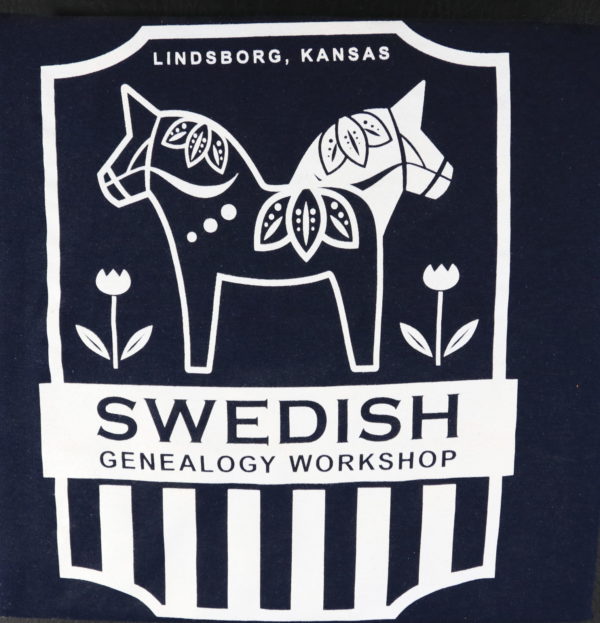 On a shield-shaped border, two stylized Dala horses - with pointed ears and leafy designs - face opposite directions. To their left and right are stylized tulips. Wording reads: "Lindsborg, Kansas. Swedish Genealogy Workshop."