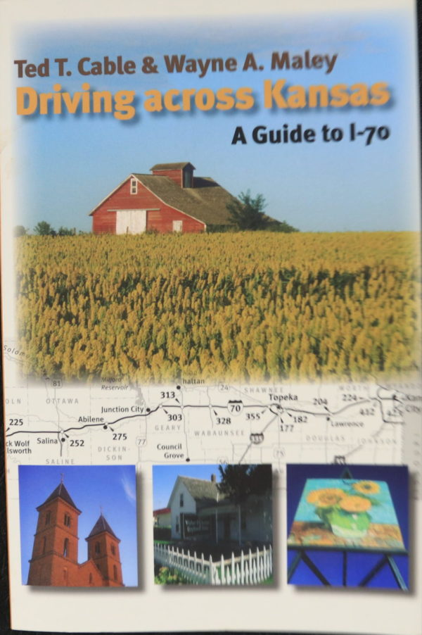On this cover, multiple images in a mosaic. The main image at top is a red barn with brown roof across a yellow field of crops. Three small pictures are along the bottom: Two tall red towers, a white house behind a picket fence, a VanGogh painting reproduction on a tall billboard from a low angle. Behind everything is a black and white road map of I-70 through Kansas.