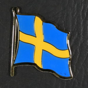 A small metal magnet in the shape of the Swedish flag, waving in the wind - a yellow cross on a light blue background.