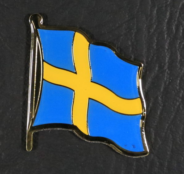 A small metal magnet in the shape of the Swedish flag, waving in the wind - a yellow cross on a light blue background.