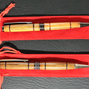 Two light-colored wooden pens with metal accents, resting on a red sleeve.