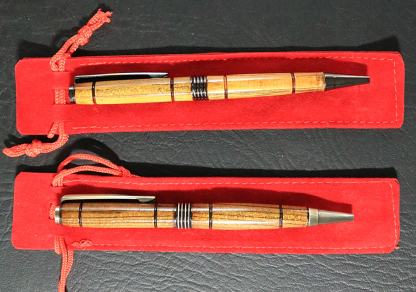 Two light-colored wooden pens with metal accents, resting on a red sleeve.
