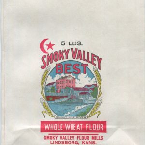 A large, flat unused flour bag in full color. At the center in an oval frame is a view of a red brick, three-story mill building with a gabled roof, surrounded by lower level industrial buildings. In the foreground is a blue river that has been dammed. On either side of the frame are stalks of yellow wheat. The label at the bottom reads "Smoky Hill River." To the upper left is a red crescent moon and star. Text on the bag reads: "5 pounds. Smoky Valley Best. Whole Wheat Flour. Smoky Valley Flour Mills. Lindsborg, Kansas."