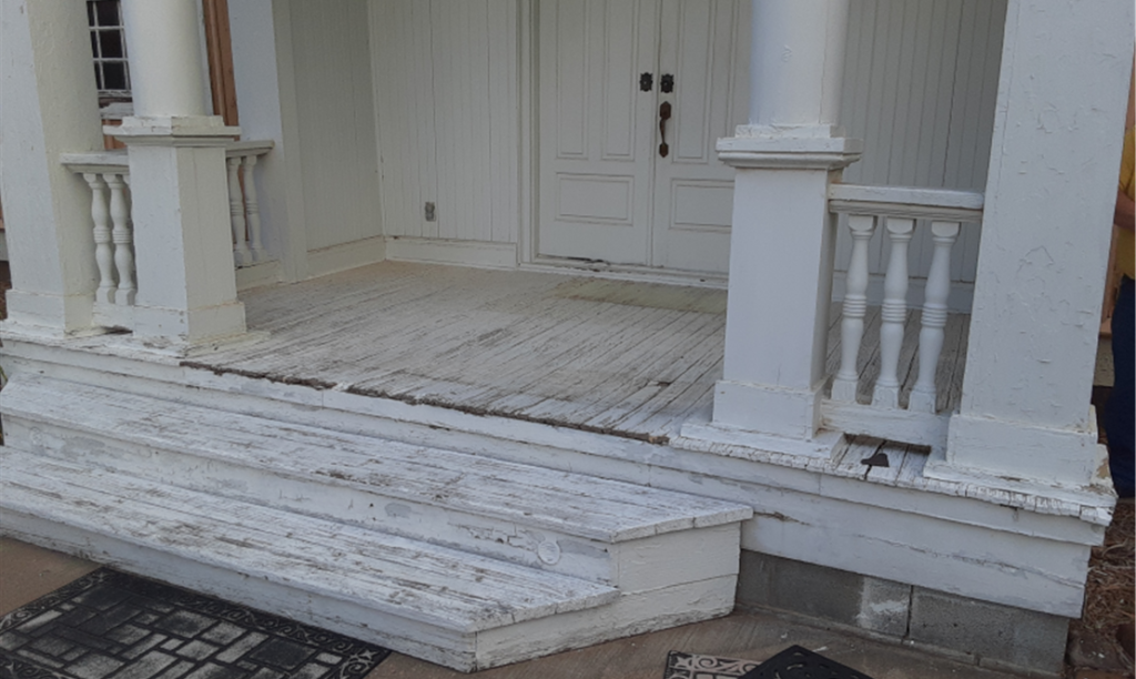 A white porch with two steps leading to it, with two large white pillars framing it and a low railing.